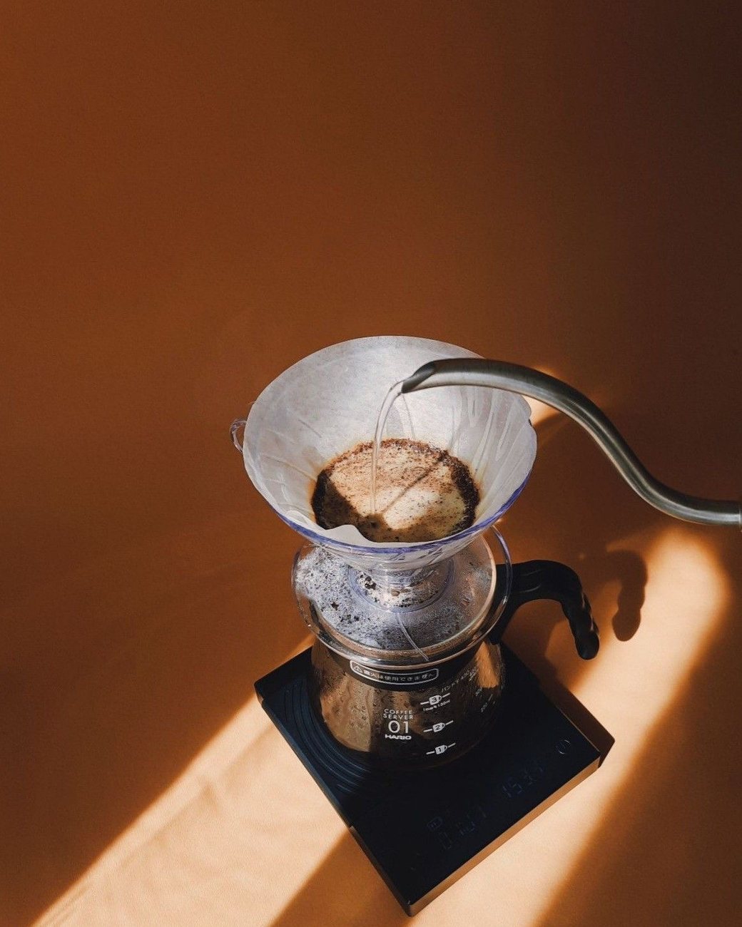 Café sendo coado no filtro sobre a balança, com luz de sol no fim da tarde